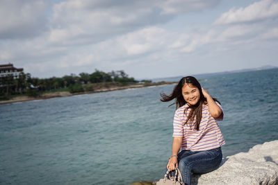 Portrait of smiling young woman standing in sea against sky