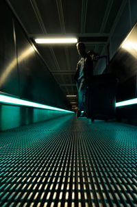 Man standing with luggage on illuminated moving walkway