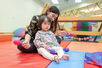 Cute girl with teacher playing on carpet in kindergarten