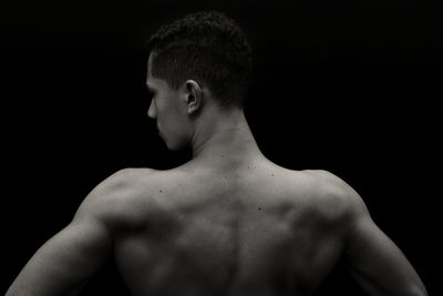 Rear view of shirtless man looking away against black background