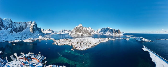 Panaromic aerial shot of isolated fishing valley against clear sky, surrounded by snowy mountains