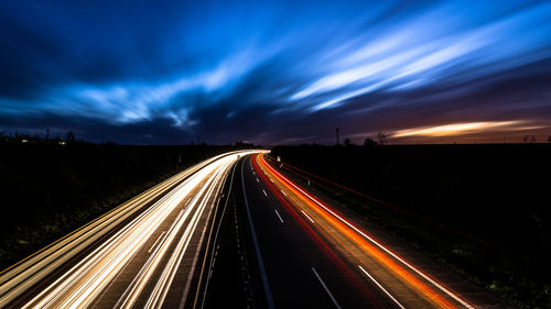 Light trails on road against cloudy sky at night