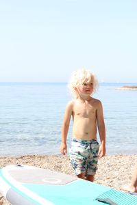 Cute shirtless boy standing by surfboard at beach