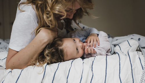 Happy mother playing with daughter while lying on bed at home