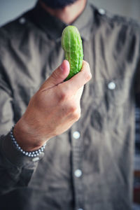 Midsection of man holding cucumber