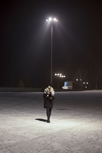 Rear view of woman standing on street light at night