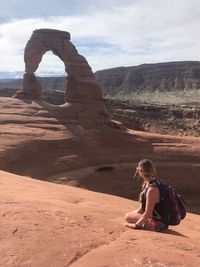 Woman sitting on rock against sky