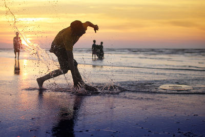 Boy splashing water at seashore during sunset