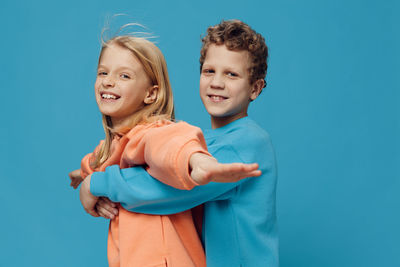 Boy embracing girl with arms outstretched from behind against blue background