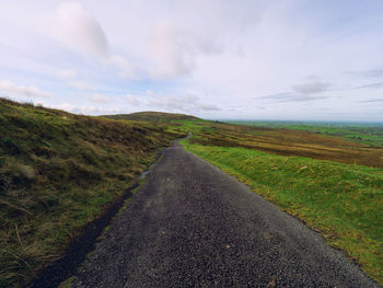 Road amidst field against sky