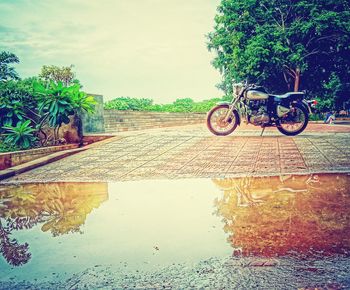 Bicycle on wet road against sky during rainy season