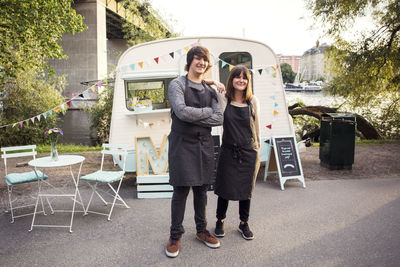 Full length portrait of confident owners standing on street against food truck