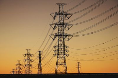 Low angle view of silhouette electricity pylon against sky during sunset