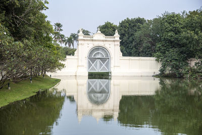 Reflection of building and trees by lake against sky