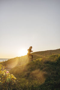 Side view of mature woman jogging on hill against sky at sunset