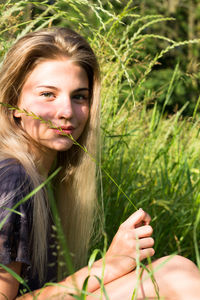 Portrait of beautiful woman with long blond hair while sitting on grassy field
