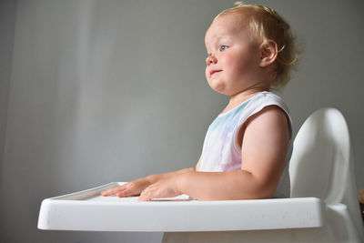 Side view of cute girl sitting in feeding chair at home, 23 months old child