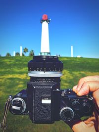 Cropped image of man holding camera against lighthouse