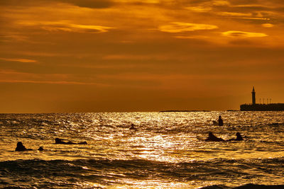 Scenic view of sea with silhouette people against sky during sunset