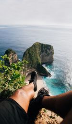 Midsection of man on rock by sea against sky