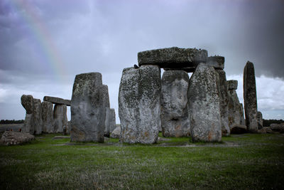 Stone structure on field against cloudy sky