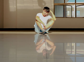 Portrait of young man sitting on tiled floor with reflection