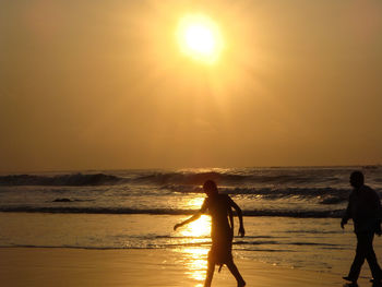 Silhouette people on beach against sky during sunrise 