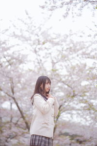 Young woman looking away while standing on tree