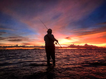 Silhouette man fishing in sea against sunset sky