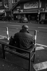 Rear view of man sitting on bench in city