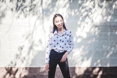 Portrait of smiling young woman standing against wall