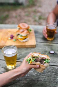 Cheeseburger in an unrecognizable female hand next to a glass of beer. suburban lifestyle.