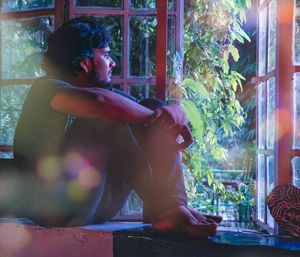 Side view of thoughtful young man looking through window at home