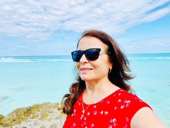 Young woman wearing sunglasses while standing at beach against sky