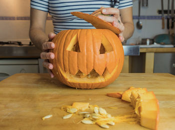 Midsection of person holding pumpkin on table at home