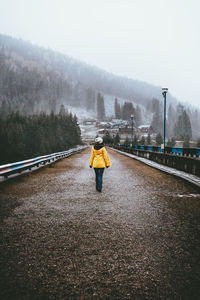 Rear view of woman walking on road during foggy weather