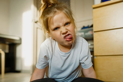 Girl 3-year-old at home on floor grimaces, makes faces at camera