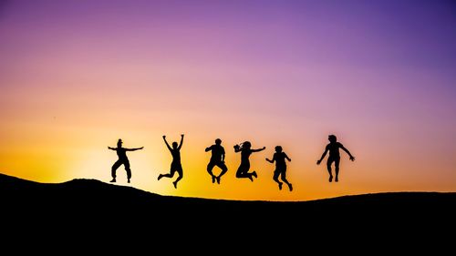 Silhouette people jumping on land against sky during sunset