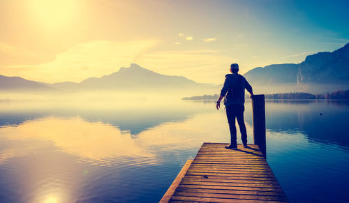 Rear view of man standing by lake on jetty