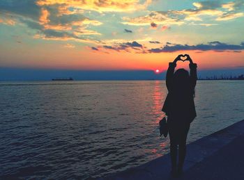 Silhouette woman forming heart shape while standing on promenade during sunset