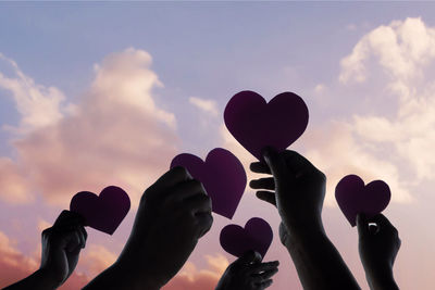 Low angle view of silhouette hand holding heart shape against sky