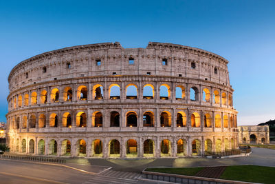 Illuminated coliseum against clear blue sky at dusk