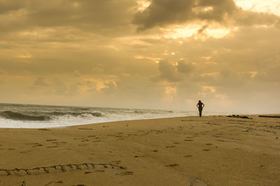 Silhouette man standing on beach against sky during sunset