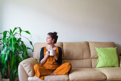 Beautiful woman holding coffee cup sitting on sofa at home