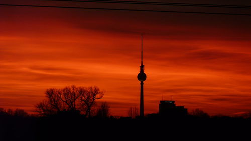 Silhouette of communications tower in city during sunset