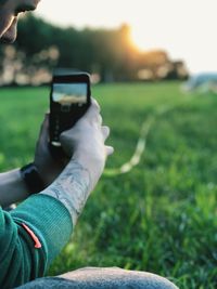 Midsection of man photographing grass field by phone