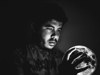 Close-up of man holding illuminated sphere in darkroom