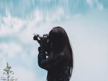 High angle view of woman photographing with digital camera against cloudy sky