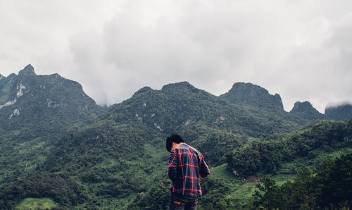 Rear view of man standing on mountain against sky