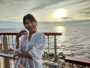 Portrait of smiling woman standing by sea against sky during sunset